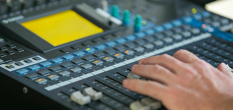 Gros plan des mains d’une personne interagissant avec une console de mixage sonore
