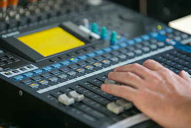 Gros plan des mains d’une personne interagissant avec une console de mixage sonore
