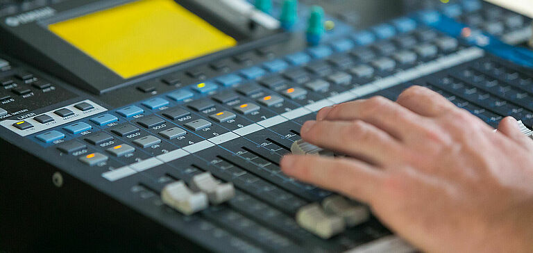 Gros plan des mains d’une personne interagissant avec une console de mixage sonore