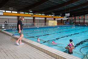 Des enfants apprennent à nager avec une maitre-nageuse au bord d'une piscine
