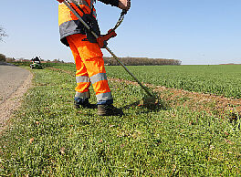 Photo d'un bord de route avec un agent coupant l'herbe avec une débroussailleuse.
