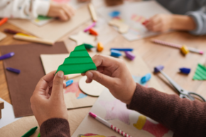 Un enfant découpe un sapin en papier.